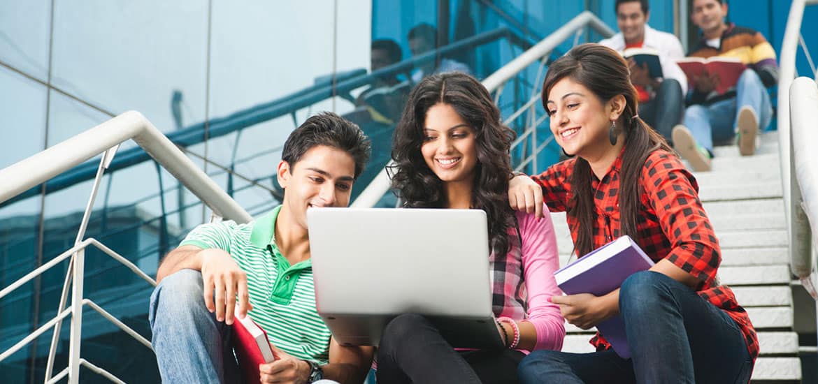 Students studying together with a laptop outside a modern educational building.