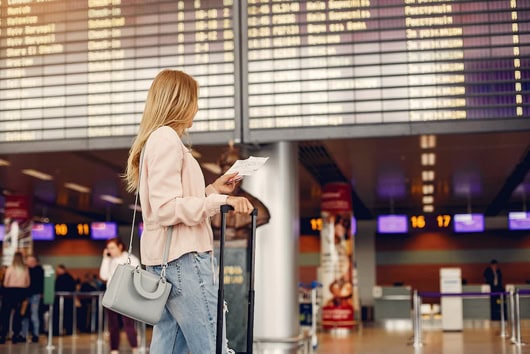 Woman with luggage checking her phone at airport terminal.