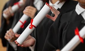 Graduates holding diplomas in black gowns with red ribbons at a graduation ceremony.