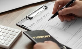 Person filling out a visa application form with a passport and calculator nearby.