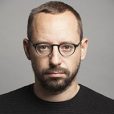Professional man with glasses, focused expression, gray background.