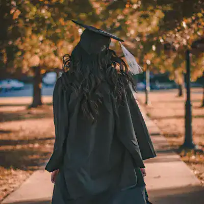 Graduate in cap and gown celebrating academic achievement outdoors.
