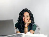 Smiling woman studying IT certifications on her laptop at a desk.
