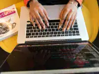 Hands typing on a laptop keyboard with certification materials nearby.