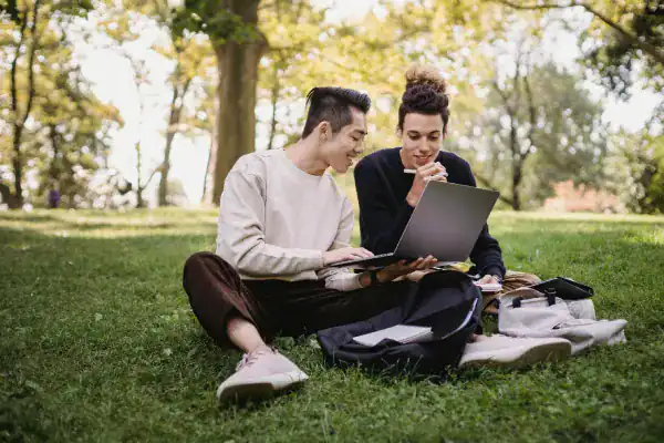 Two young women studying IT certifications outdoors on a laptop.