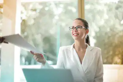 Woman smiling with documents in a bright office setting.