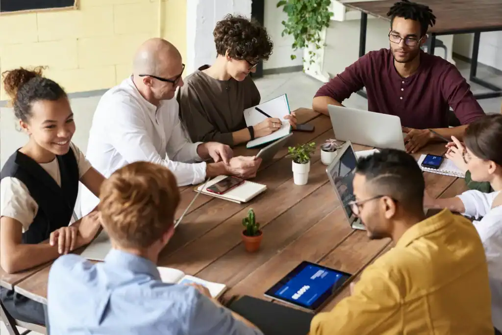 Diverse group of professionals collaborating around a table with laptops and tablets.