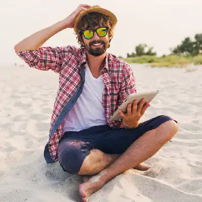 Happy man with sunglasses using tablet on the beach, promoting Azure Data Engineering.
