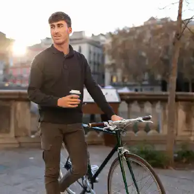 Young man standing with bicycle outdoors in urban park during sunset.