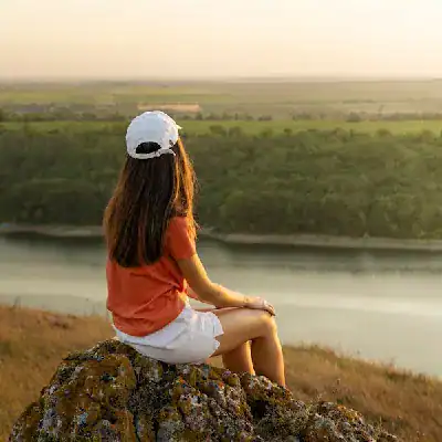 Young woman sitting on a rock overlooking a river, contemplating her Salesforce certification journe.