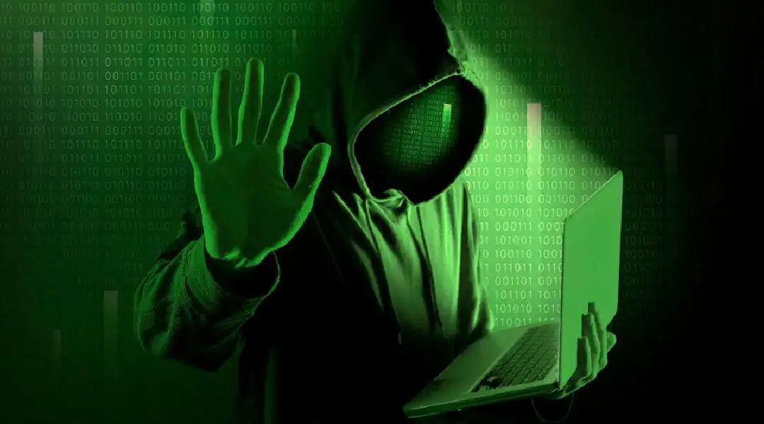 Hacker in hoodie using laptop with green digital background.