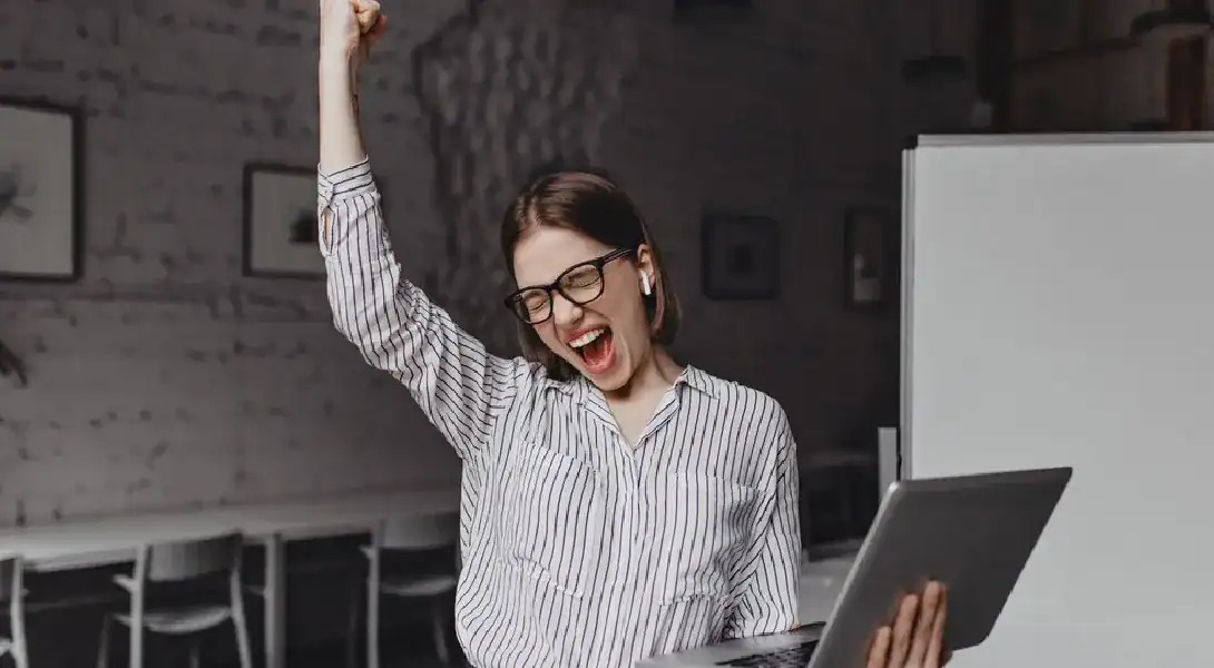 Woman celebrating success with laptop after renewing Microsoft AZ-900 exam.