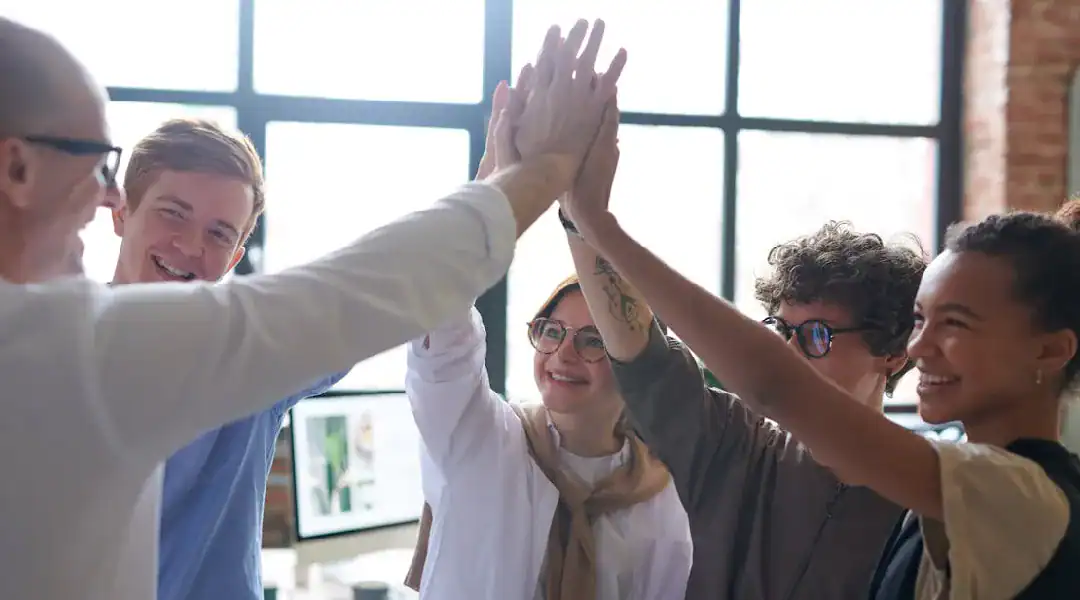 Group of diverse professionals giving a high-five in a modern office setting.