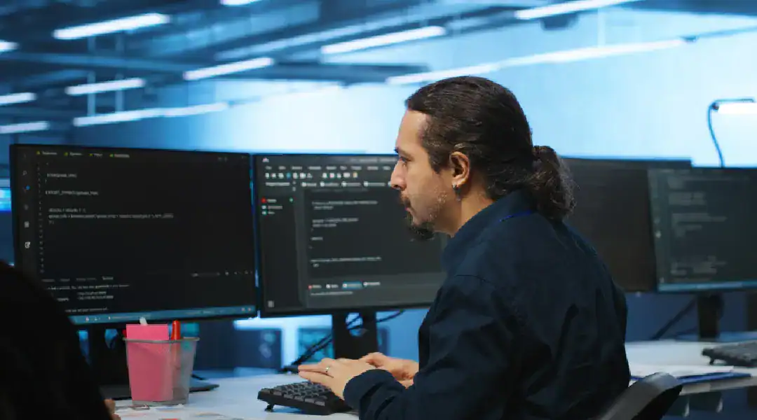 An IT expert working on cybersecurity coding and analysis in a modern office environment.