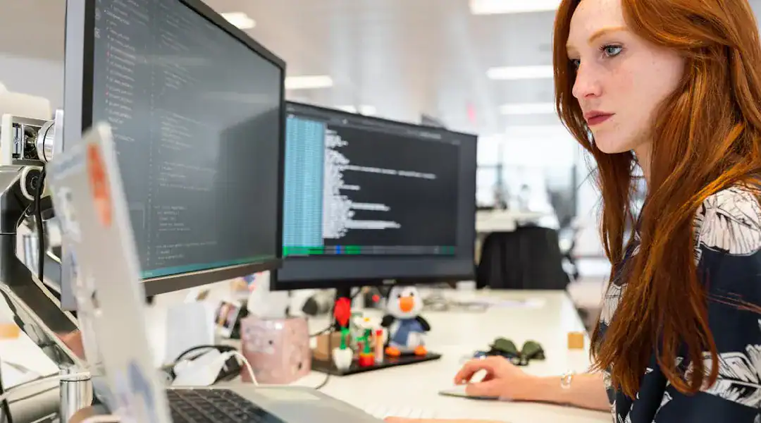 Woman working on coding and network automation on dual monitors in an office setting.