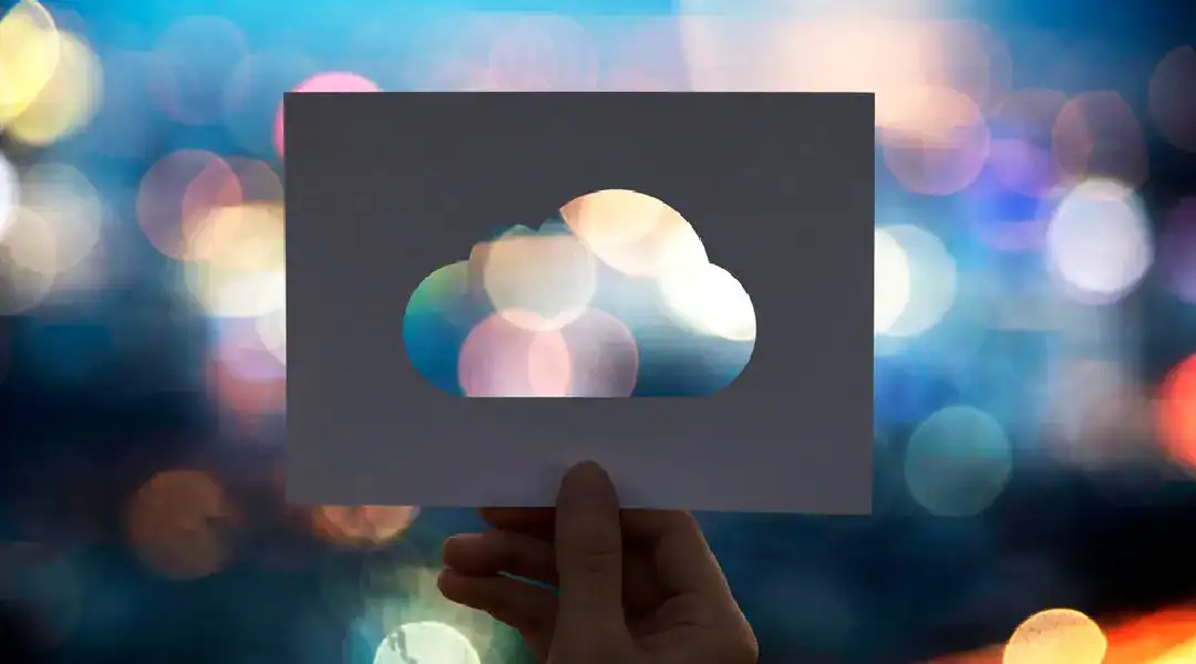 Cloud computing concept with a hand holding a paper cutout of a cloud against a colorful bokeh backg.