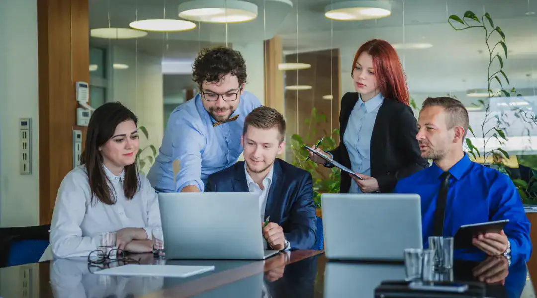 Group of professionals collaborating around laptops in a modern office setting.