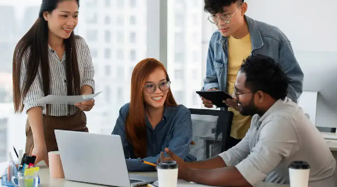 Group of diverse professionals collaborating around a laptop in an office setting.