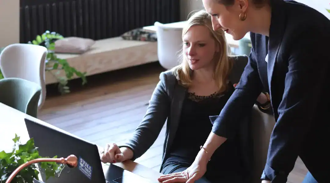 Two women collaborating on a laptop for IT certification success.