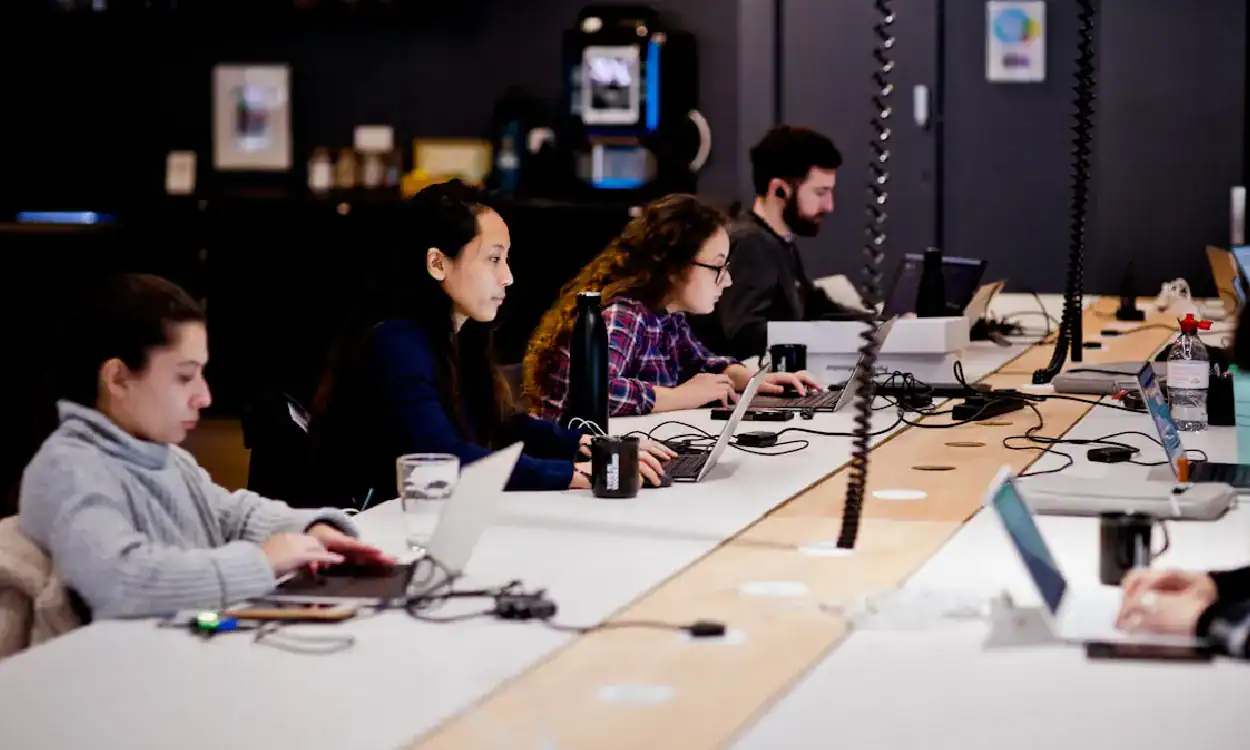 Group of students working on laptops in a tech training room.