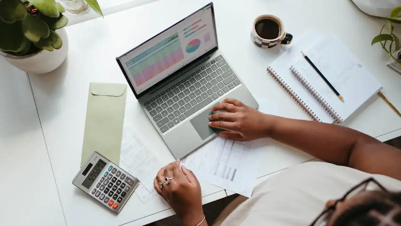 Person working on a laptop with charts, notebooks, and coffee on a white desk.